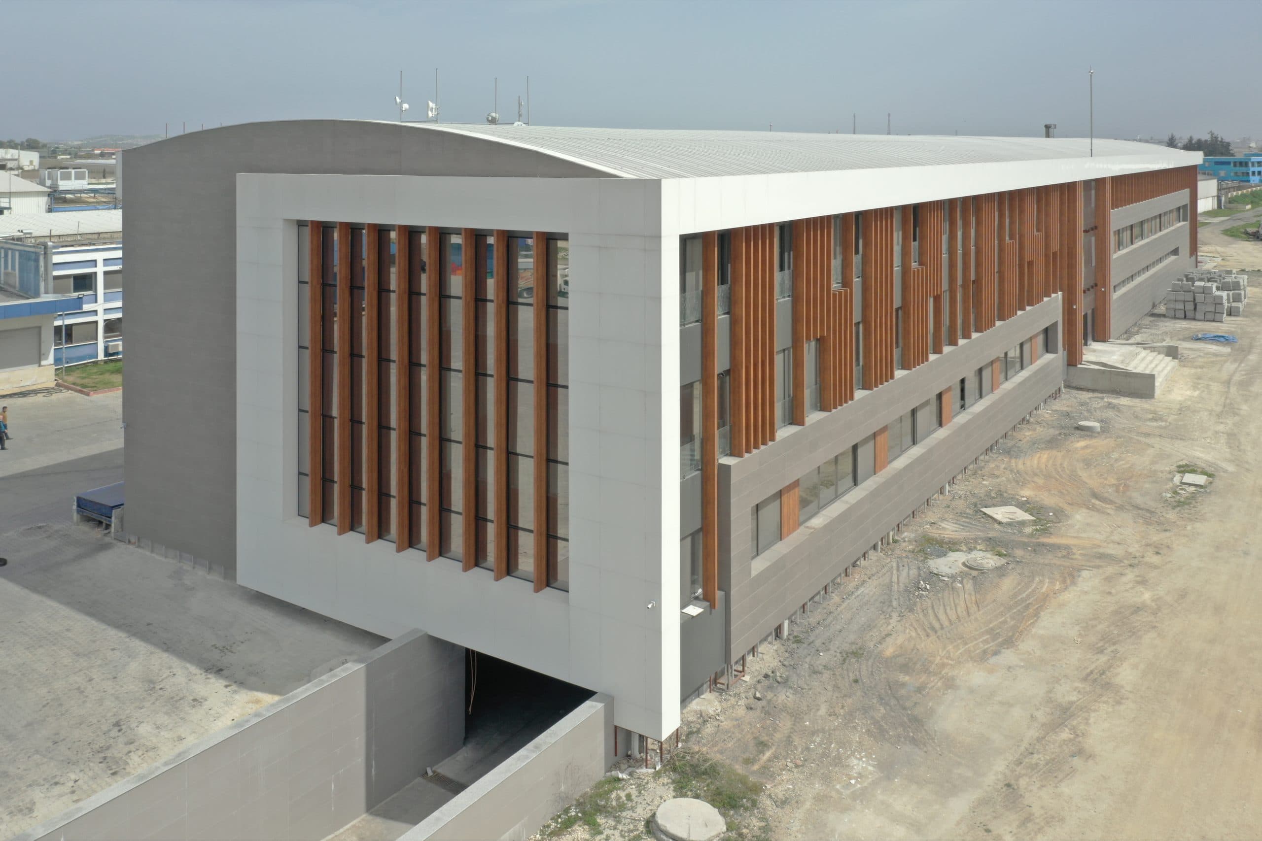 Akyem idari binası havadan: beyaz panel çerçeve, ahşap desenli dikey lameller ve gri panel bantlı uzun cephe