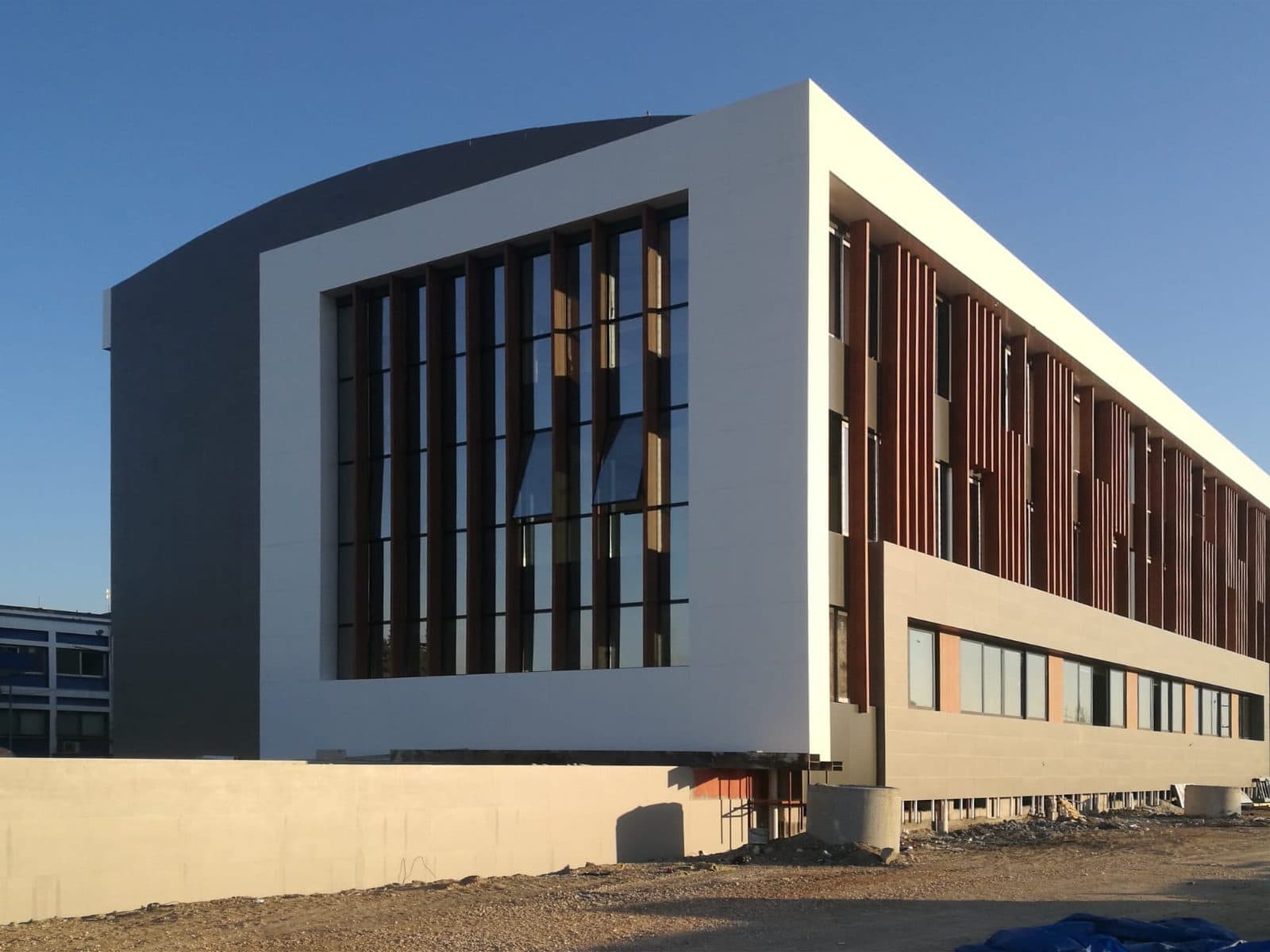 Akyem binasının uç cephesi gün batımında: beyaz çerçeve içinde cam giydirme cephe ve ahşap desenli lameller
