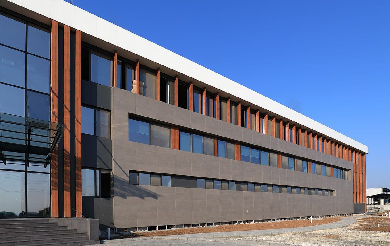 Akyem idari binasının uzun cephesi: gri panel bant içinde şerit pencereler, üstte ahşap desenli lameller