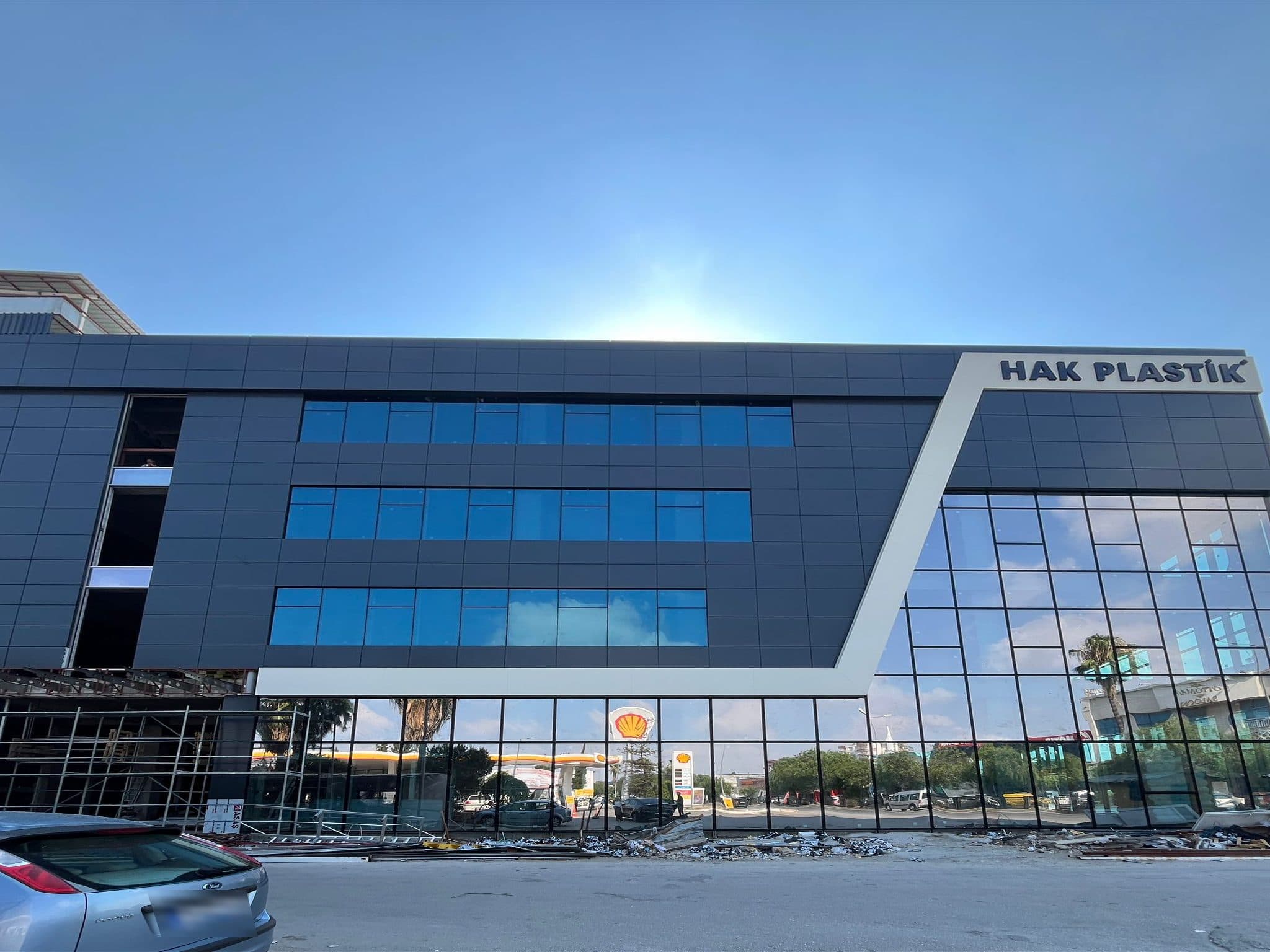 Hak Plastik binası cepheden: lacivert kompozit panel, beyaz çapraz bant ve köşede cam giydirme cephe