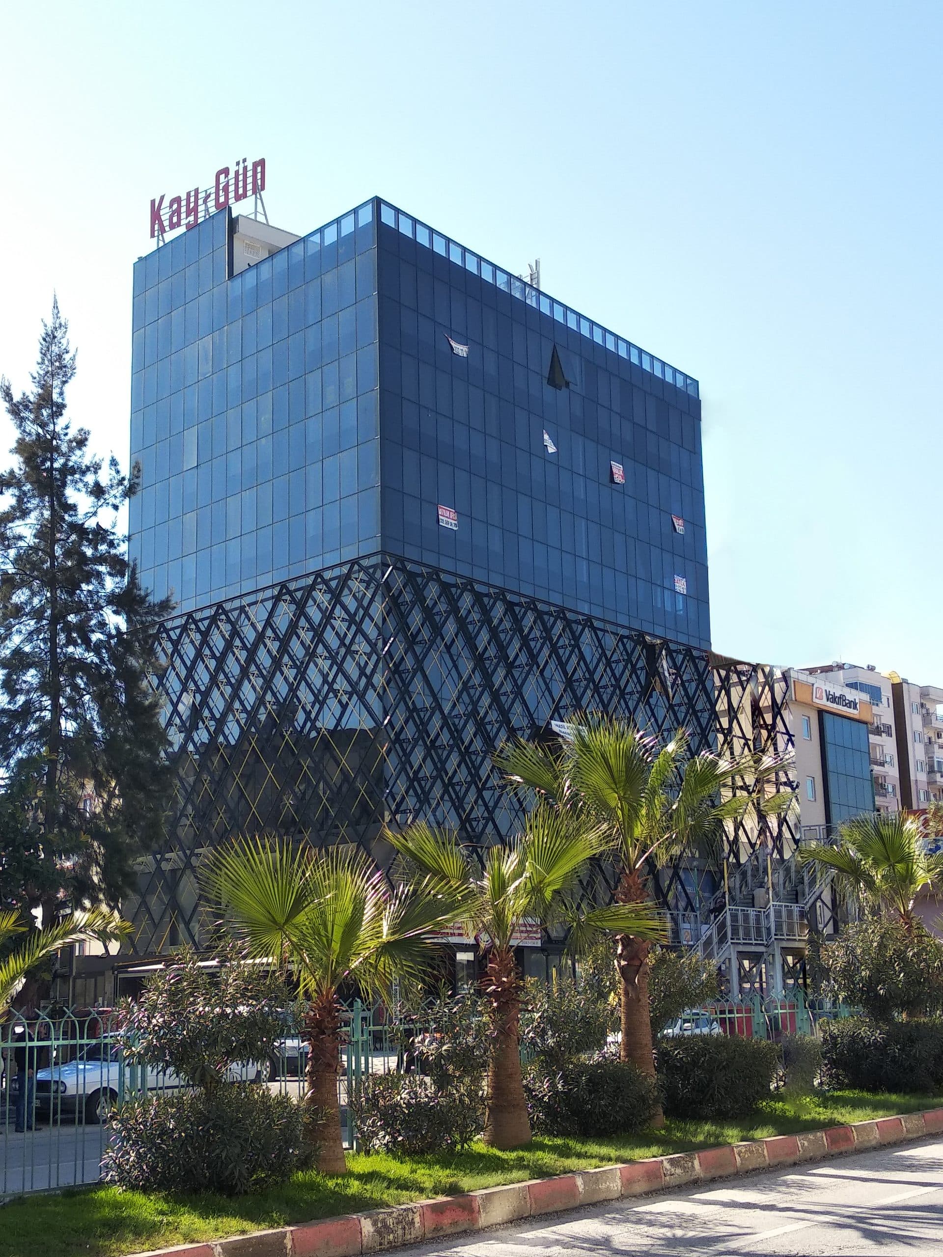 Kayıkçıoğlu Next Office: mavi silikon cam cephe ve elmas desenli dış kafes, önde palmiyeler