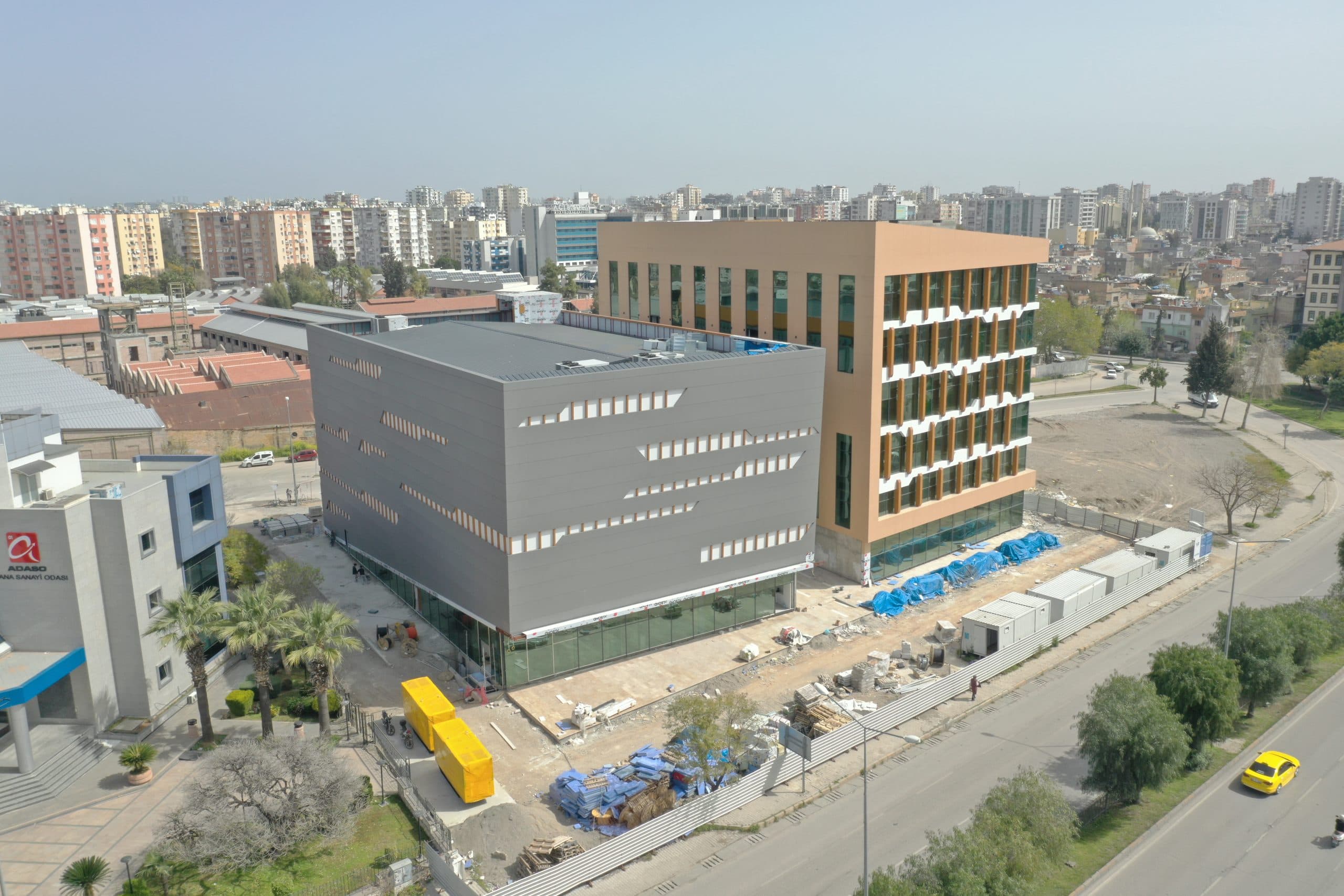 ATO gri ek bloğu havadan: şerit boşluklu antrasit kompozit panel cephe, arkada cam blok