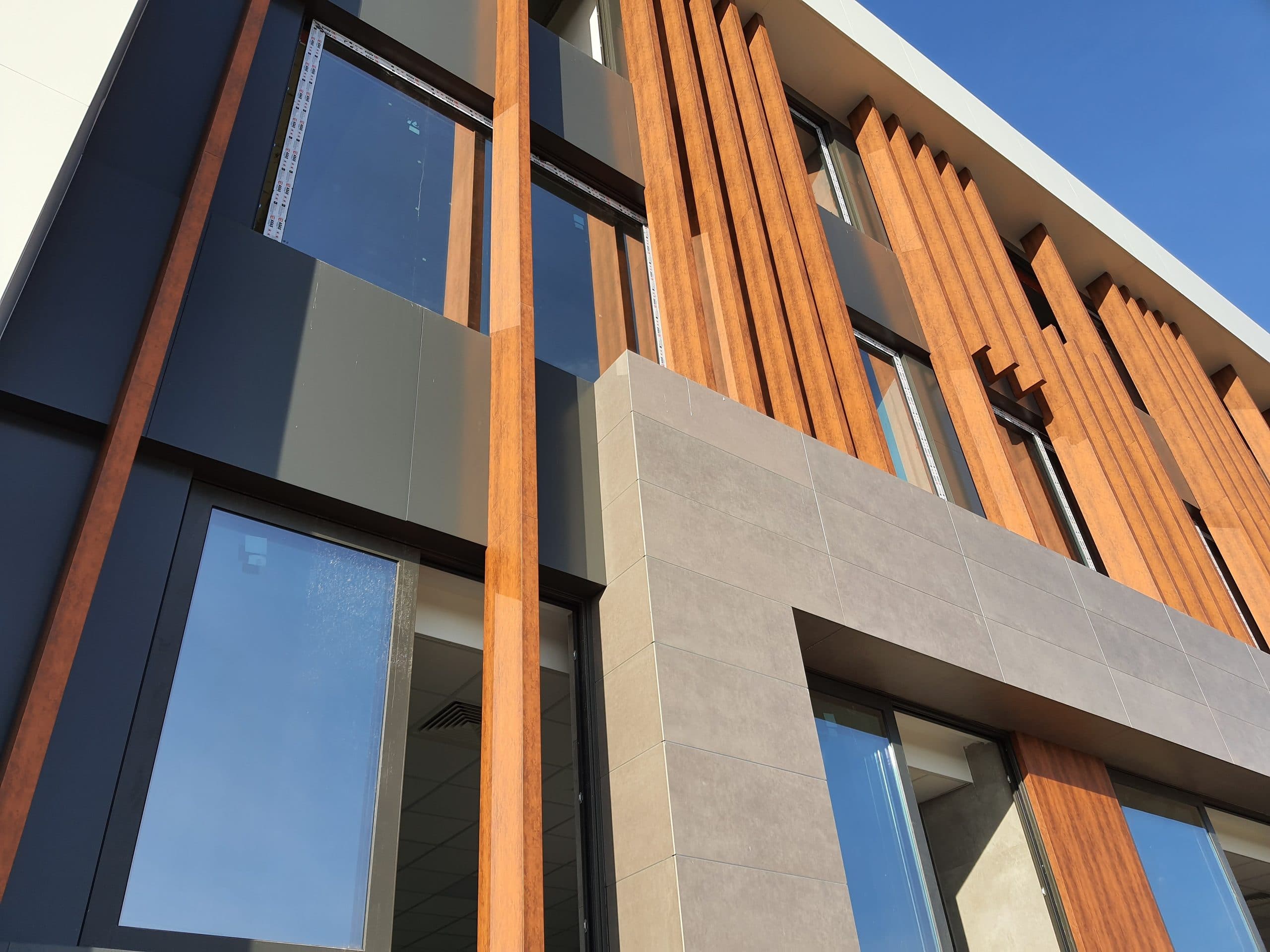 Yakın plan: ahşap desenli lameller, antrasit kompozit panel, gri taş desenli panel ve alüminyum pencere