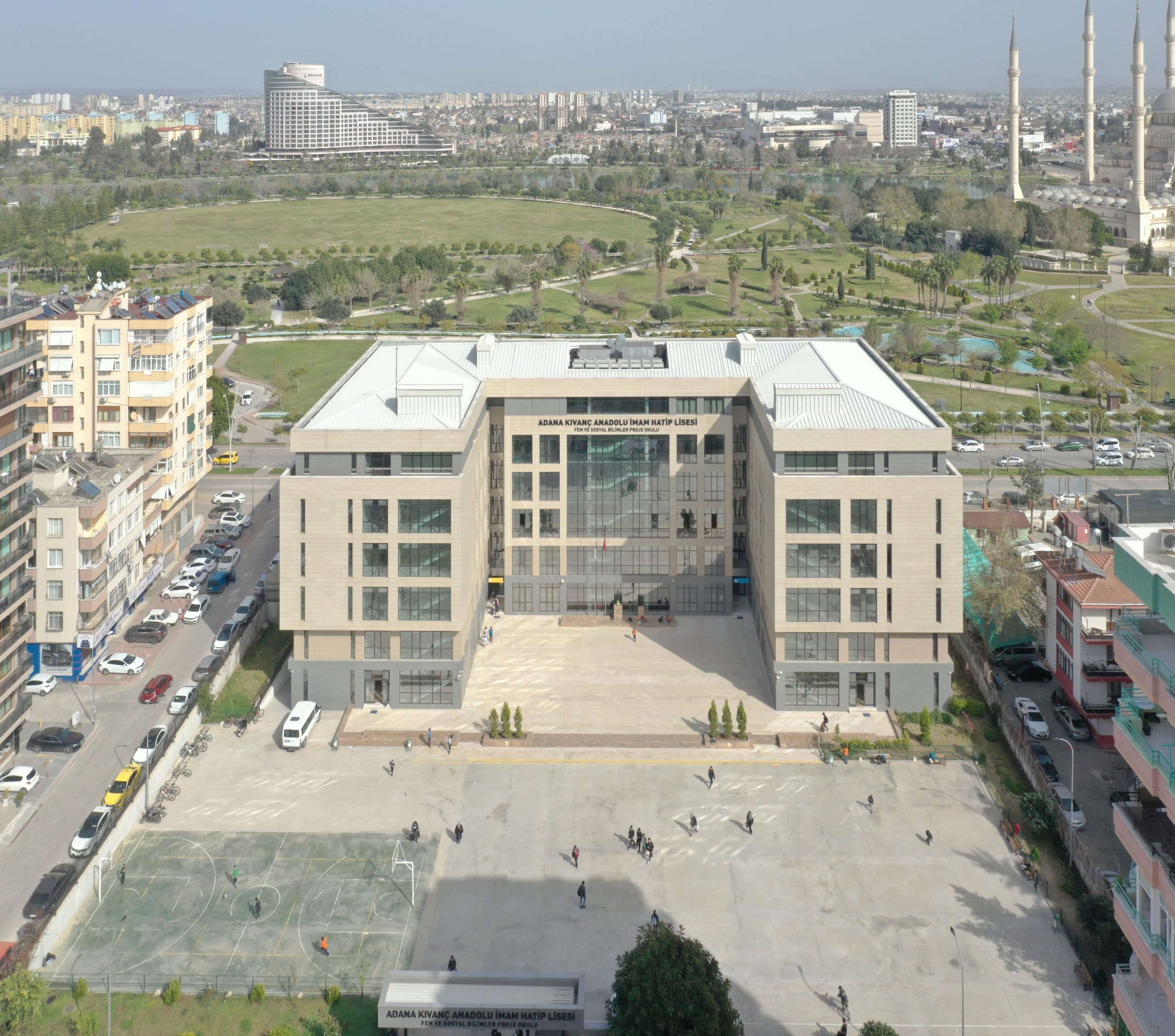 Kıvanç Anadolu İmam Hatip Lisesi'nin ön cephesi kuşbakışı; arkada Merkez Park, sağda cami minareleri