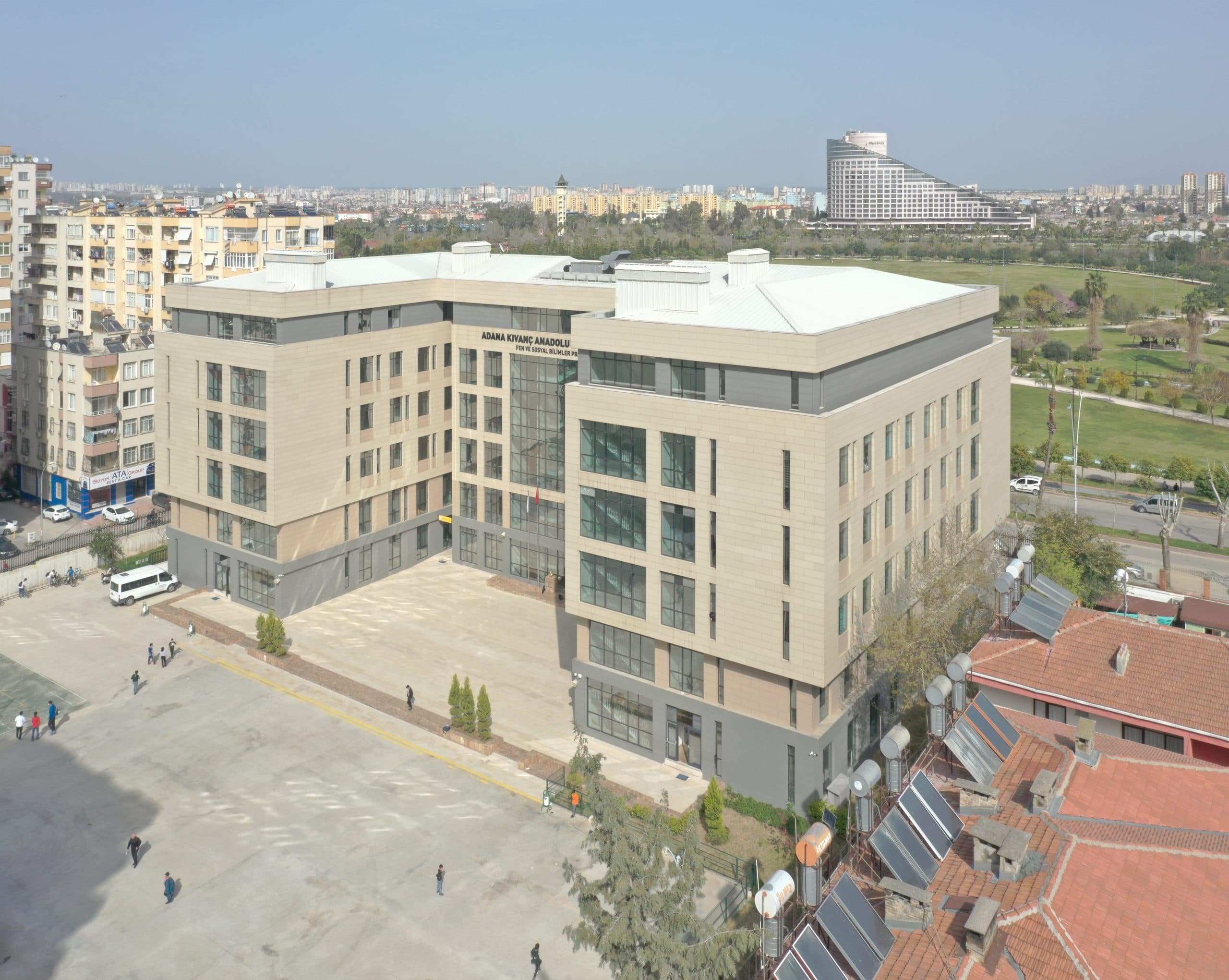 Okul binasının yan kanadı ve köşesi havadan; taş kaplama cephe ve cam atriyum