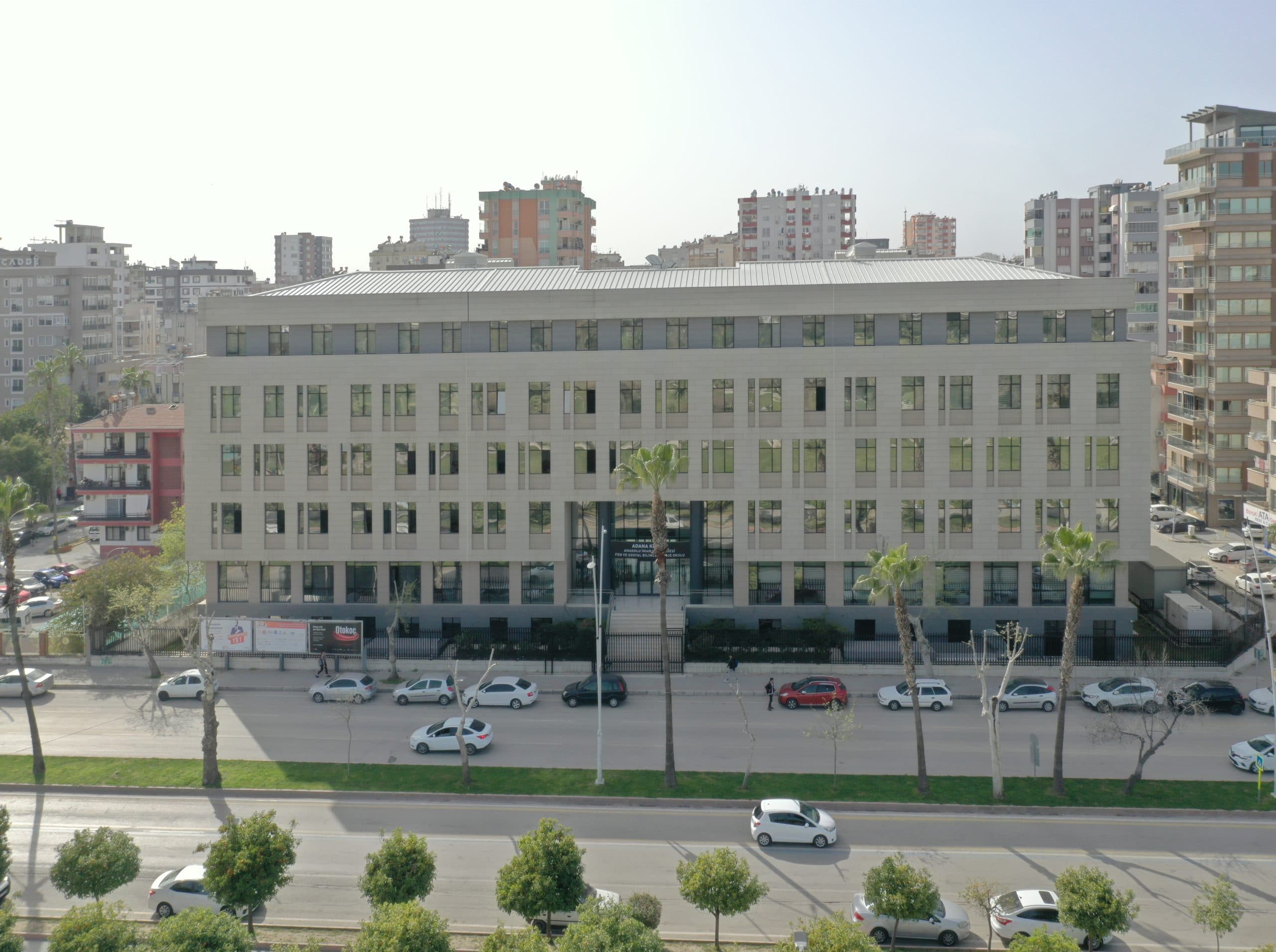 Okulun cadde cephesi karşıdan, havadan; düzenli pencere ritmi ve taş görünümlü kaplama