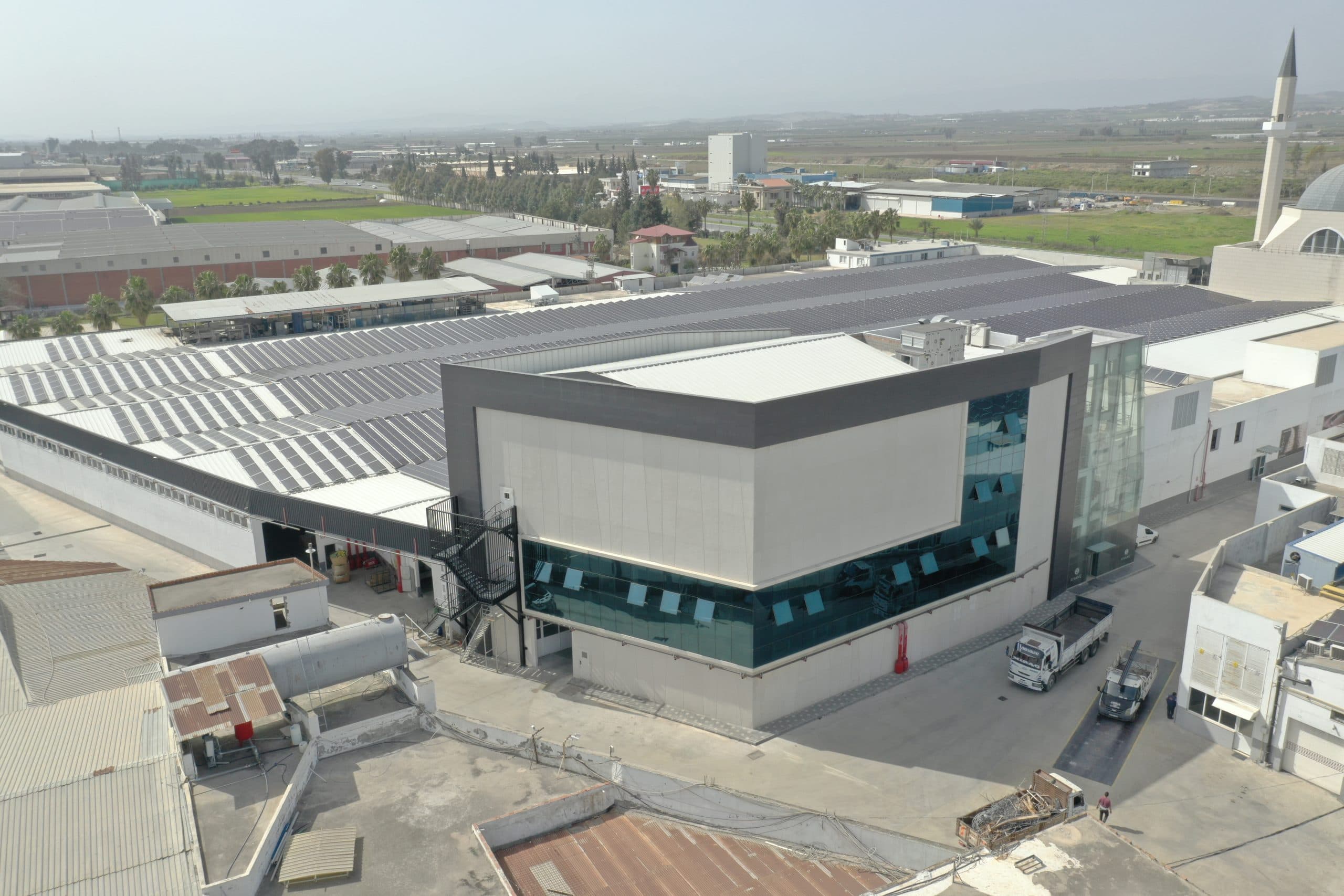 Kıvanç Tekstil ofis bloğu: antrasit çerçeveli beyaz paneller, şerit cam cephe ve köşede cam merdiven kulesi