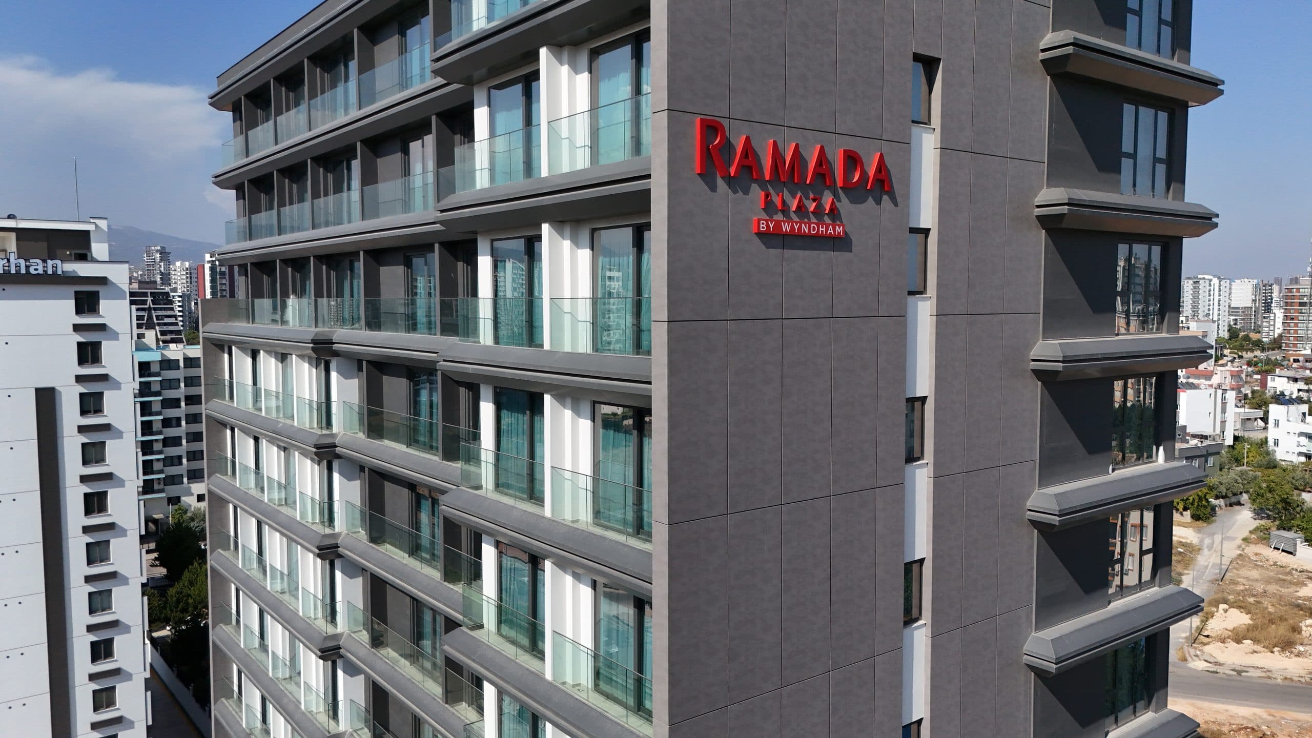 Ramada Plaza by Wyndham tabelası, büyük ebatlı gri cephe panelleri ve cam korkuluklu balkonlar yakın plan